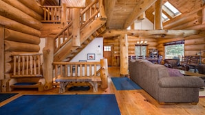 A log cabin interior with a wooden staircase, a living area with a sofa, and a dining area with chairs and a table. - Luxury Log Cabin-Windham Mountain.  Amazing sunsets, large lawn, deck, fireplace (Windham)