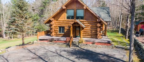 A log cabin with a porch, a stone foundation, and a surrounding wooded area.