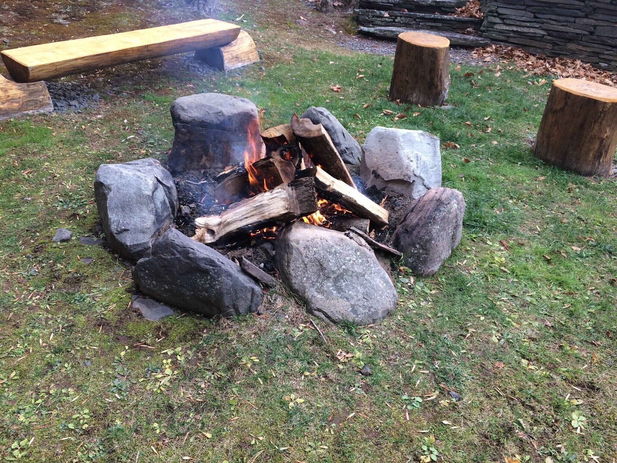 A campfire surrounded by rocks and logs on a grassy area.