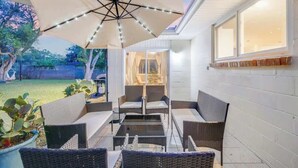 An outdoor patio with wicker furniture, a large umbrella, and a view of the backyard. - Huge Yard with Marsh Views! | Minutes to Beach/DT! (St. Augustine)