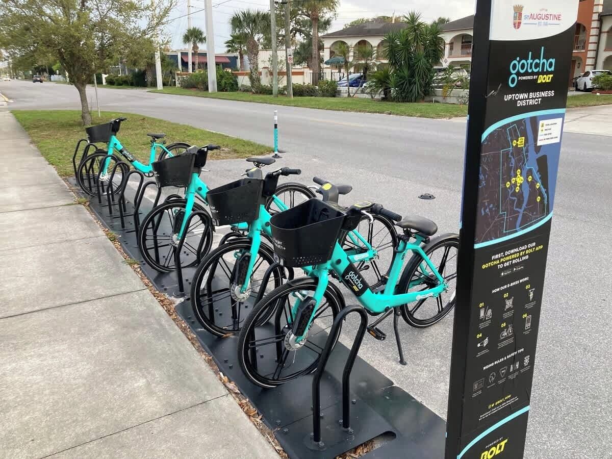 Une rangée de vélos de couleur turquoise est stationnée à côté d’une station de vélos en libre-service, où l’on trouve une carte et des instructions.
