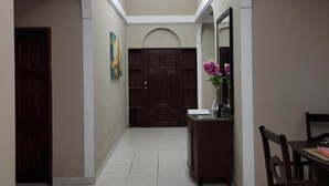 A spacious hallway with a high ceiling, a chandelier, a wooden door, and a dining area with a table and chairs.