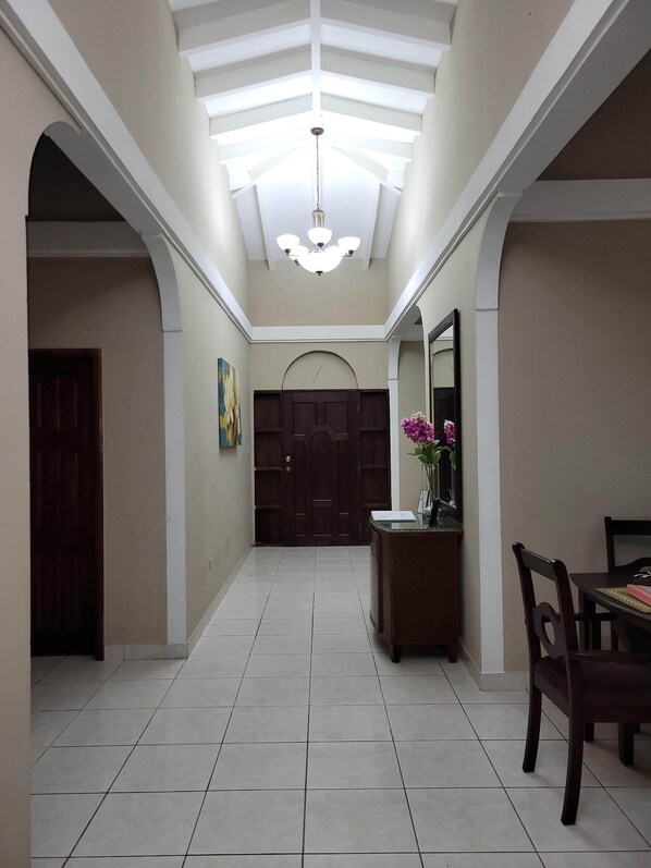 A spacious hallway with a high ceiling, a chandelier, a wooden door, and a dining area with a table and chairs.