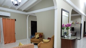 A spacious living area with a sofa, armchairs, and a wooden cabinet.
