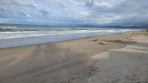 A beach with waves, a cloudy sky, and distant mountains.