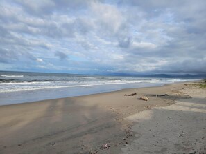 Una playa con olas, un cielo nublado y montañas a lo lejos.