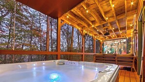 Un bain à remous sous une pergola en bois, illuminé de guirlandes lumineuses, et entouré d’arbres.