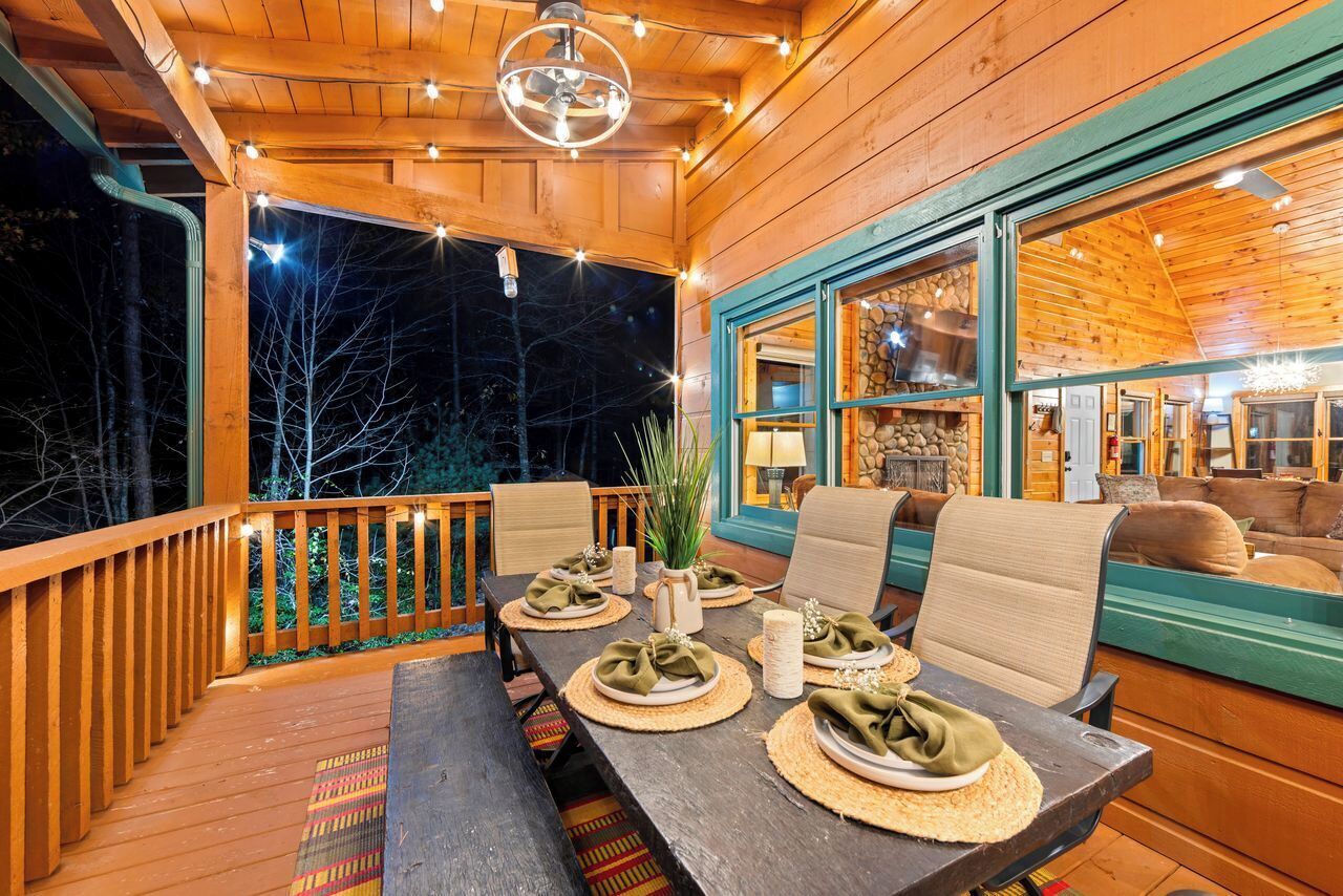 Eine HolzdTerrasse mit Esstisch, gedeckt für vier Personen, umgeben von Stühlen und Blick ins Innere durch große Fenster.