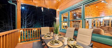 Eine HolzdTerrasse mit Esstisch, gedeckt für vier Personen, umgeben von Stühlen und Blick ins Innere durch große Fenster.
