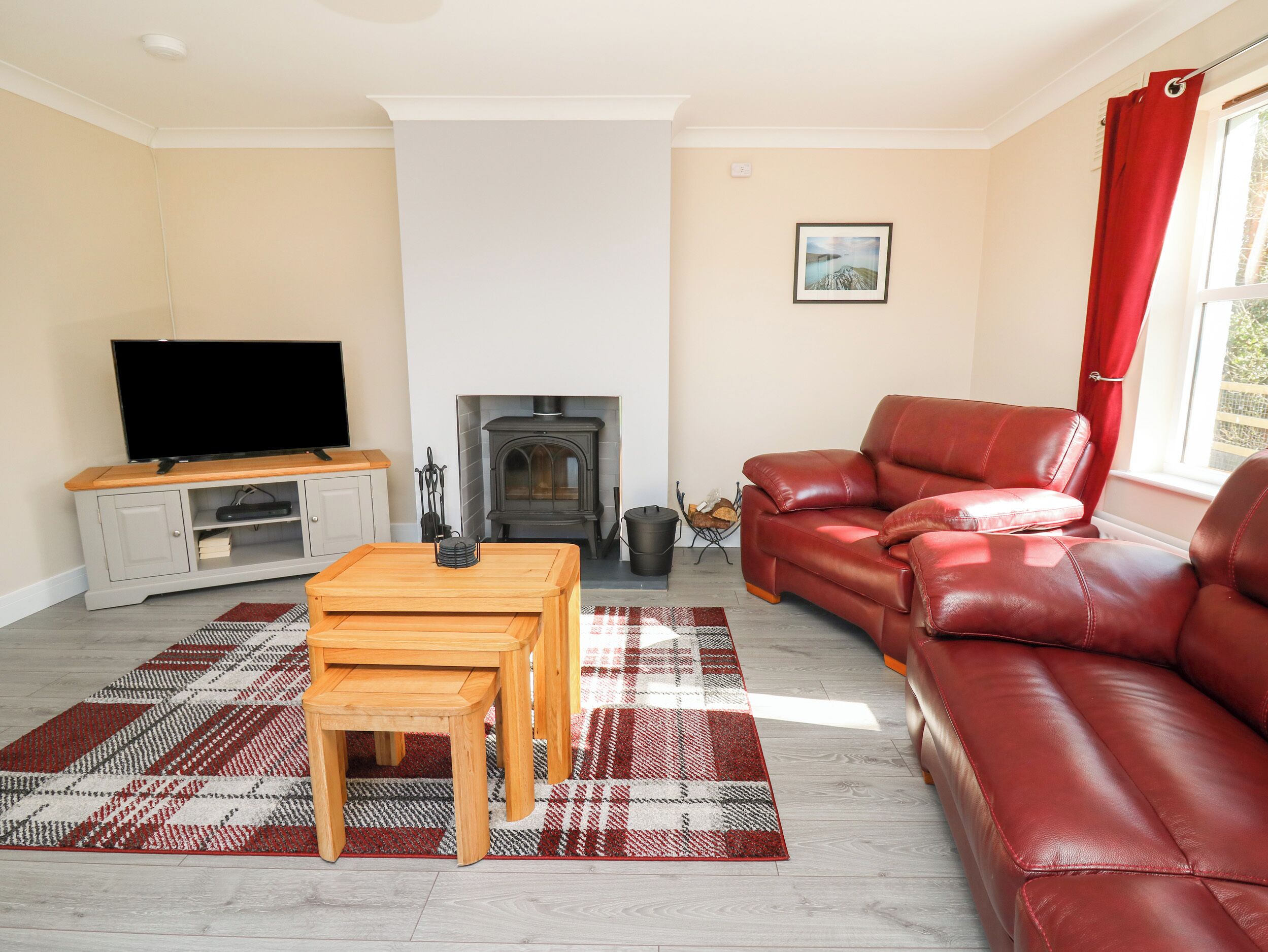 A living room with a fireplace, a red leather sofa, a wooden coffee table, and a television on a cabinet.
