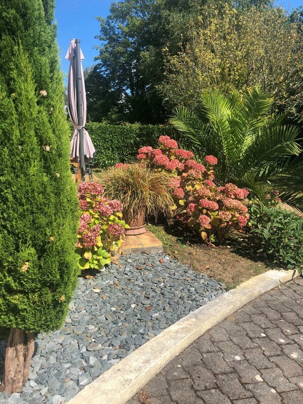 Ein Garten mit Kiesweg, verschiedenen Pflanzen und einer überdachten Sitzgelegenheit im Freien.