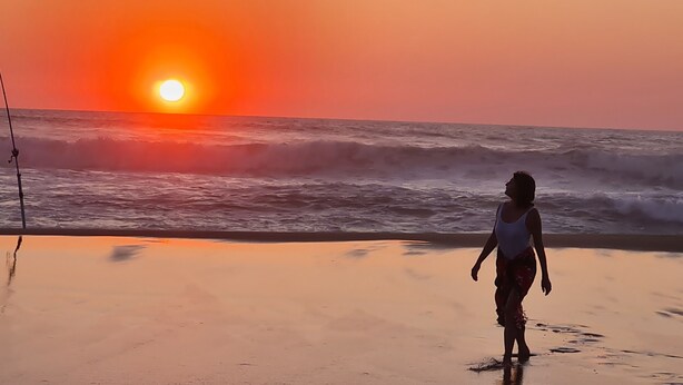 Une scène de plage avec un coucher de soleil, des vagues et une personne qui se promène.