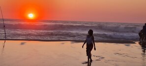 A beach scene with a sunset, waves, and a person walking.
