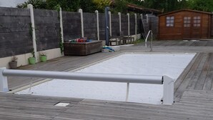 Une terrasse en bois avec une barrière métallique, une petite structure en bois et une clôture métallique.