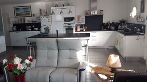 Une cuisine moderne avec des meubles blancs, un coin repas doté d’une chaise rembourrée et un vase rempli de fleurs.