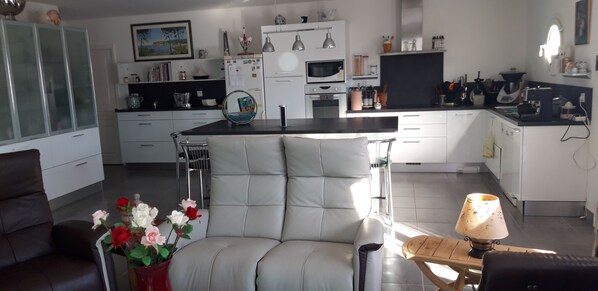 A modern kitchen with white cabinets, a dining area with a cushioned chair, and a vase of flowers.