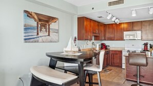 Eine moderne Küche mit Holzschränken, ein Essbereich mit rundem Tisch und Stühlen sowie ein Gemälde eines Piers an der Wand.