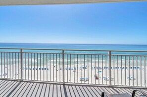 A balcony with a view of a beach, white railings, and a clear blue sky.