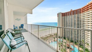 Un balcon avec des fauteuils en osier, une piscine et une vue sur la plage et l’océan.