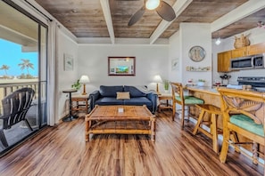 A living room with a sofa, coffee table, dining table, chairs, and a kitchen area with a microwave and stove.