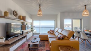 Ein modernes Wohnzimmer mit großem Fernseher, einer Couch und einem Essbereich mit Meerblick.
