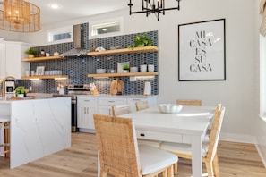 Une cuisine moderne avec des meubles blancs, un îlot en marbre et un coin repas doté de chaises en osier.