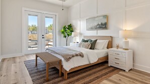 A bedroom with a large bed, a nightstand, a bench, and a view through a sliding door.