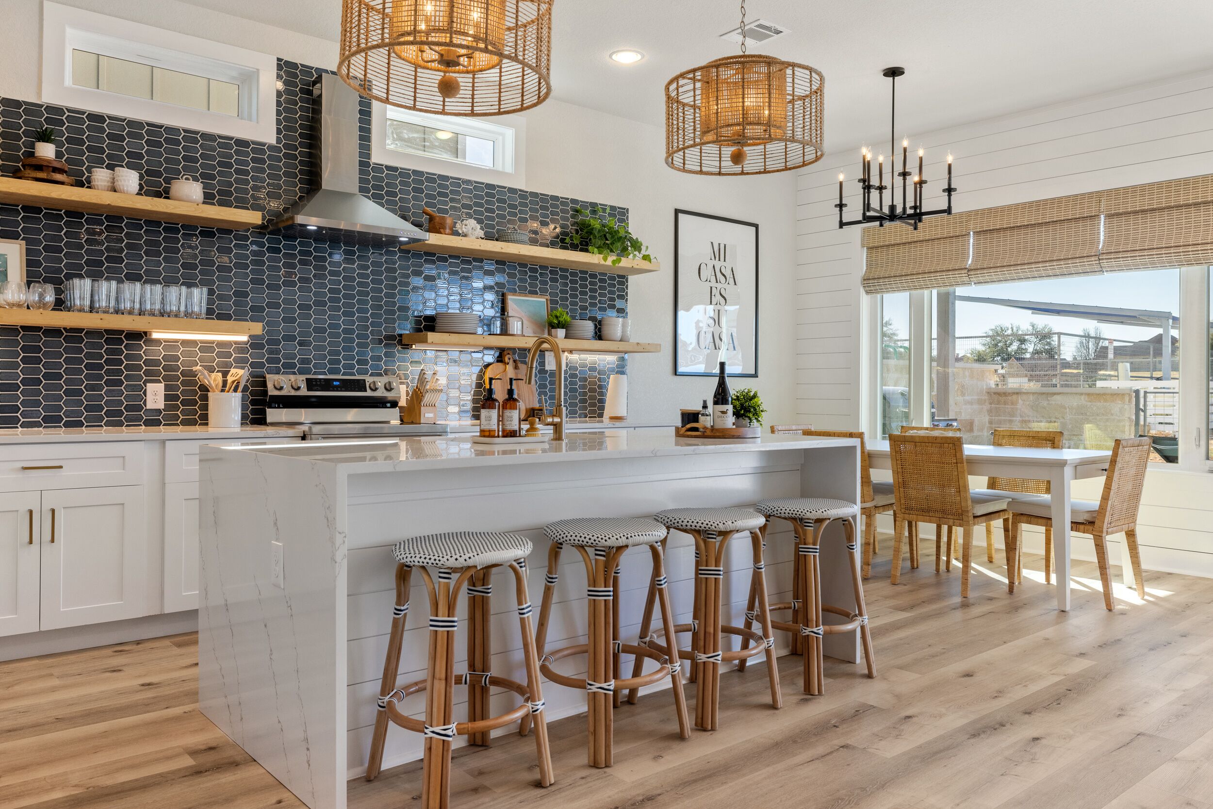 A modern kitchen with a central island, wooden stools, and a dining area with a large window.