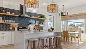 A modern kitchen with a central island, wooden stools, and a dining area with a large window.