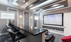 Un salón de conferencias con una larga mesa, sillas negras, una pantalla de proyector y una puerta blanca.