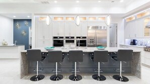 Een moderne keuken met witte kasten, een centraal eiland met barkrukken en roestvrijstalen apparatuur.