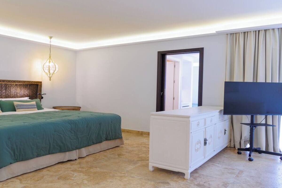 Quarto de hotel com cama grande, televisão, cômoda e janela com cortinas.