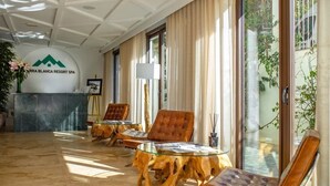 Eine Lobby mit einer Rezeption, Ledersesseln, einem Glastisch und Blick auf Grünflächen.