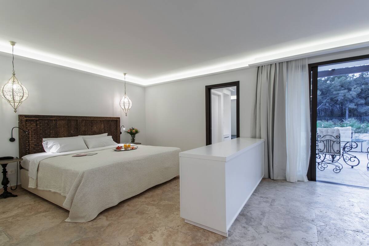 Quarto moderno com uma cama grande, mesa de cabeceira e vista para o exterior.