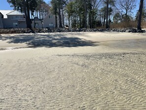 Ein sandiger Strand mit einem Haus und Bäumen im Hintergrund.