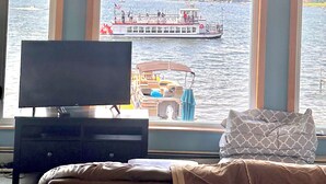 Une chambre dotée d’une grande fenêtre donnant sur un lac, d’un téléviseur posé sur un meuble et d’un lit avec un oreiller.