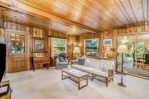 Cozy cabin-style accommodation with a seating area, sofa, armchairs, coffee table, and TV, offering a view of the surrounding greenery.