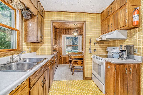 Kitchen area with double sink, stove, and coffee maker, featuring a window and door to adjacent room.