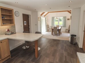 A modern kitchen with a dining area, wooden beams, and a view through the window.