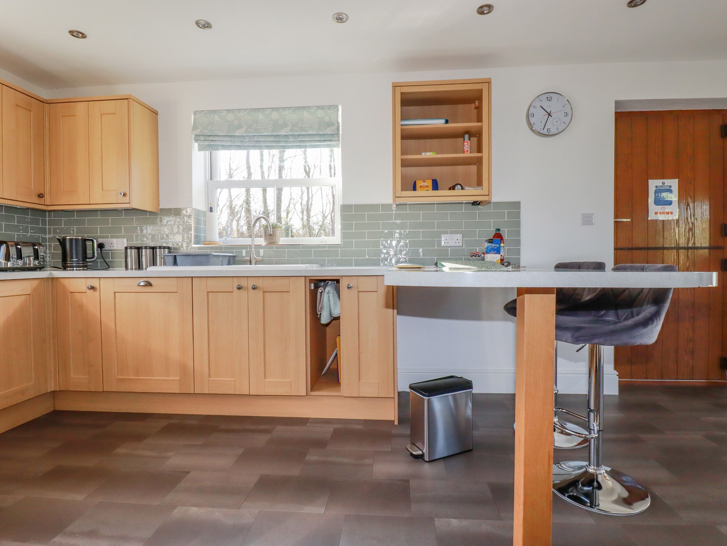 A modern kitchen with wooden cabinets, a stainless steel sink, and a window with a view of trees.