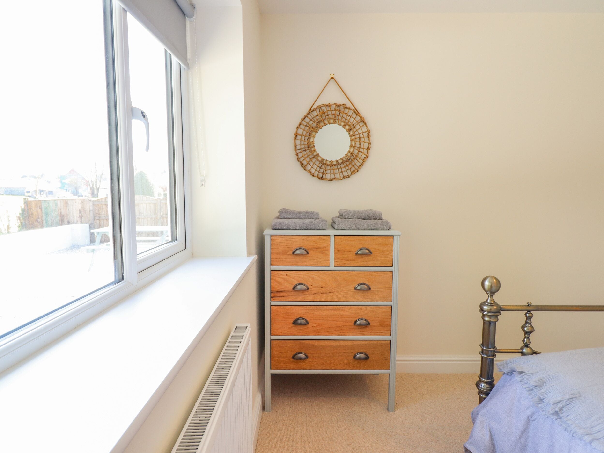 A bedroom with a window, a dresser with drawers, a bed with a headboard, and a wall-mounted mirror.