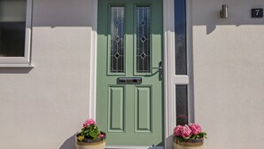 Une porte verte avec une fenêtre, une fente pour le courrier et un panneau portant le numéro 7, fixé au mur.