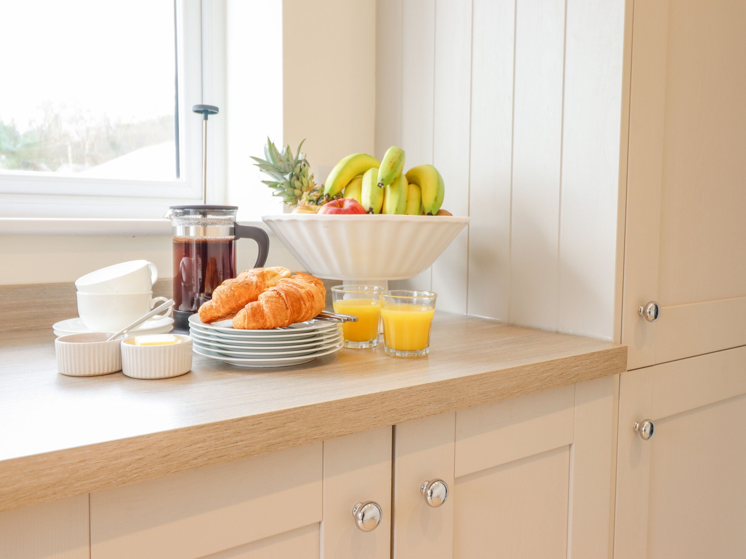 Desayuno con croissants, fruta, café y jugo de naranja sobre una encimera de cocina.