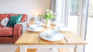 Une table à manger dressée avec de l’assiette, des bols et des couverts blancs, un vase rempli de fleurs et un canapé en cuir rouge agrémenté de coussins.