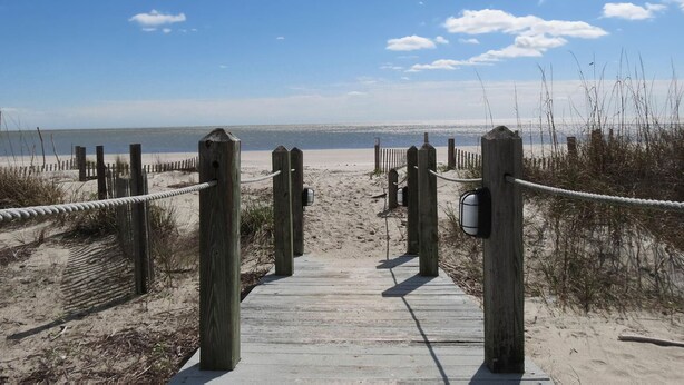 A wooden boardwalk leading to a beach with a clear sky.