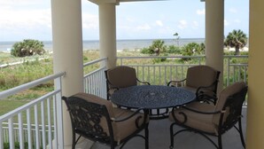 A covered outdoor seating area with a table and chairs, overlooking a beach and ocean.