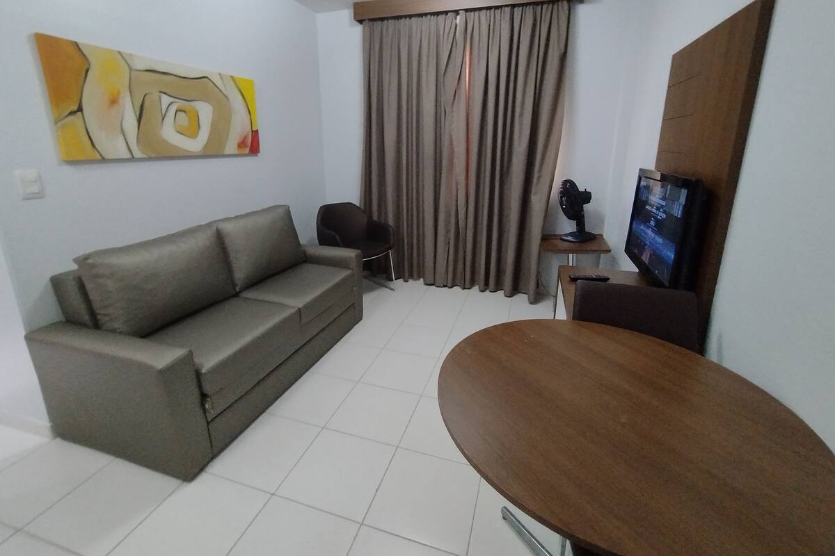 A living room with a sofa, a small table, a television, and a window with curtains.