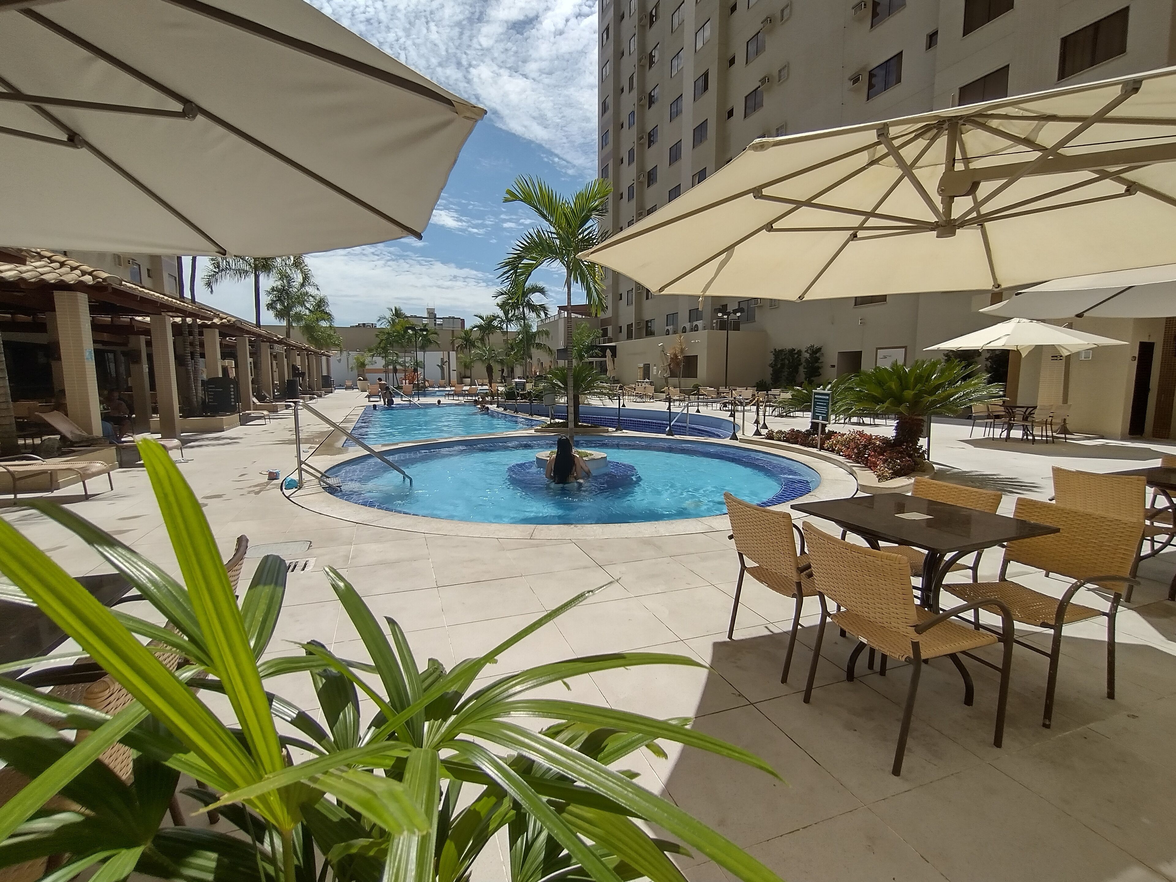 Zona de piscina con sillas de descanso y sombrillas, rodeada de edificios.