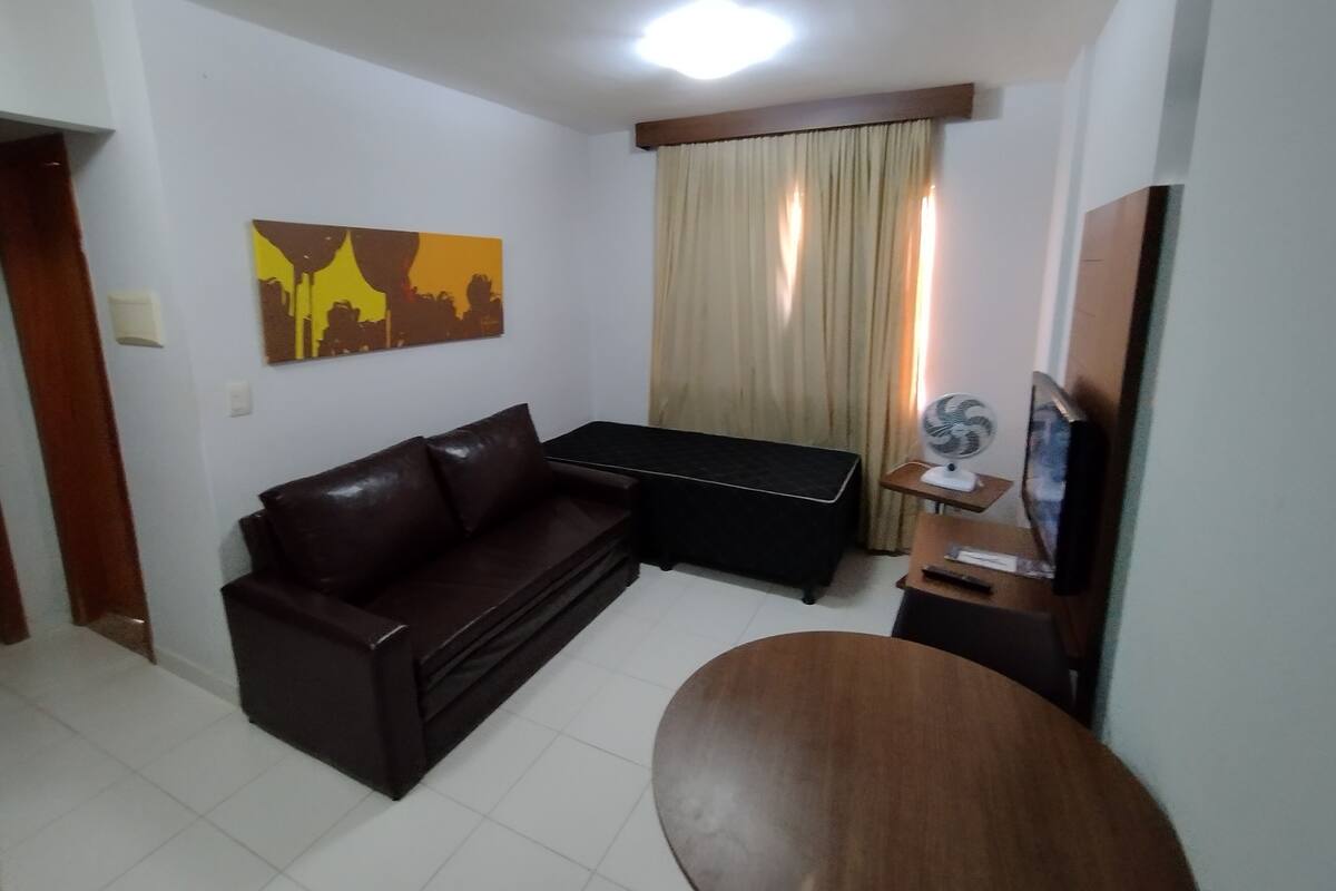A living room with a brown sofa, a wooden coffee table, a small TV on a stand, and a painting on the wall.