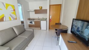 Una sala moderna con un sofá gris, una mesa de comedor con sillas, un televisor y una zona de cocina con microondas y estufa.
